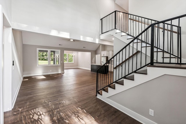 staircase featuring baseboards, a high ceiling, and wood finished floors