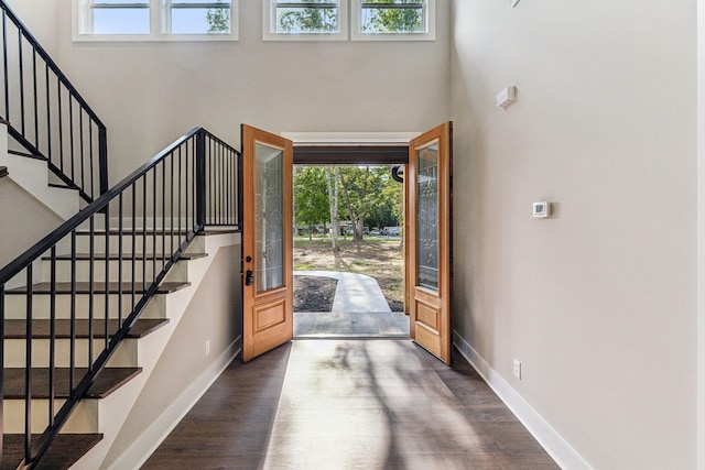 foyer entrance with a towering ceiling, baseboards, stairway, and wood finished floors