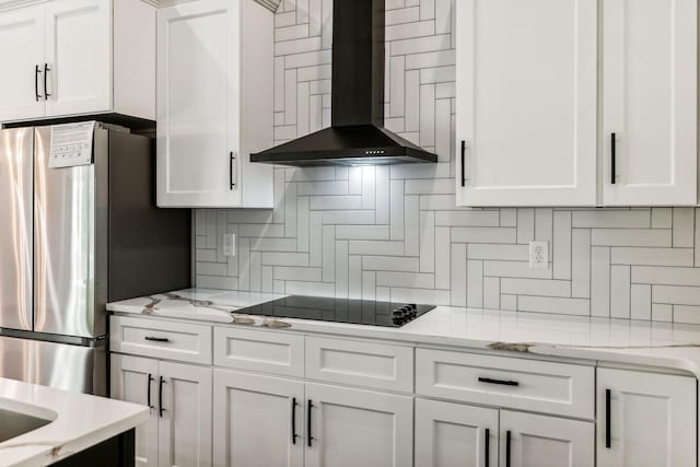kitchen with white cabinetry, wall chimney range hood, black electric stovetop, and freestanding refrigerator