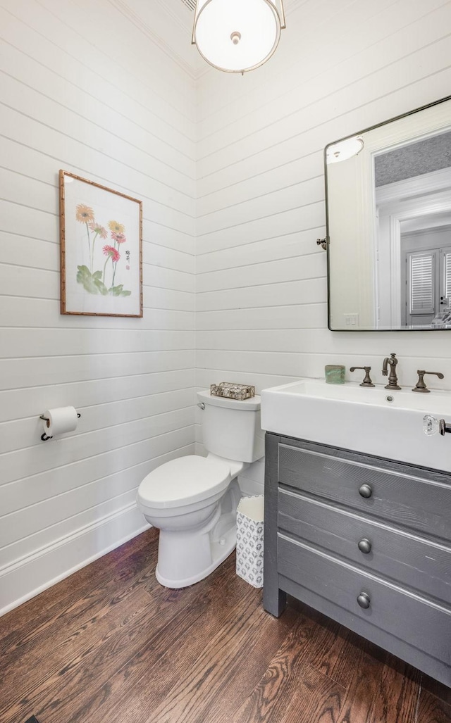 half bathroom with wooden walls, wood finished floors, vanity, and toilet