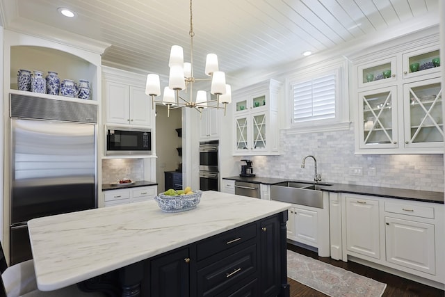 kitchen with white cabinets, built in appliances, a sink, and a chandelier