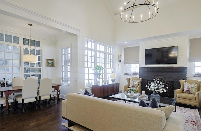 living area featuring a chandelier, a brick fireplace, a wealth of natural light, and dark wood-style floors