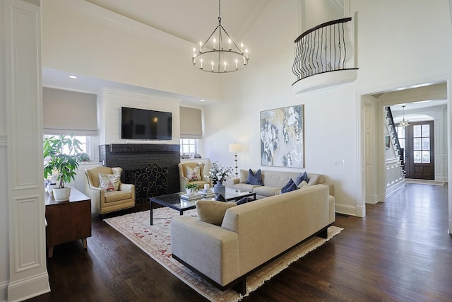 living room with an inviting chandelier, dark wood-style flooring, a brick fireplace, and plenty of natural light