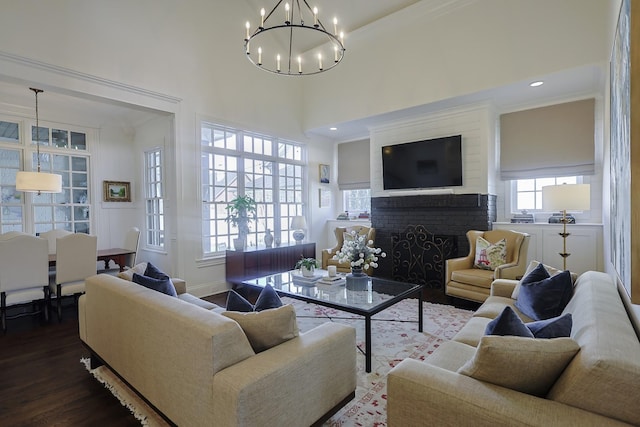 living room featuring dark wood-style flooring, a chandelier, a high ceiling, ornamental molding, and a brick fireplace