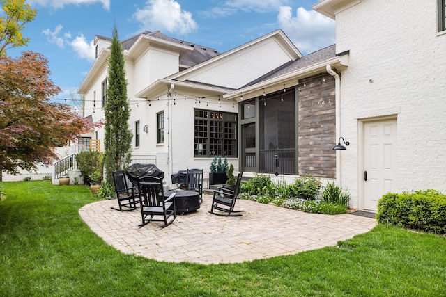 back of house featuring a lawn, brick siding, a patio area, and an outdoor fire pit