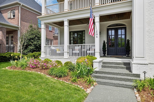 entrance to property with brick siding, a porch, a balcony, and french doors