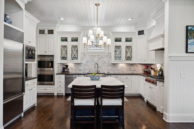 kitchen featuring white cabinets, built in appliances, a notable chandelier, and a sink