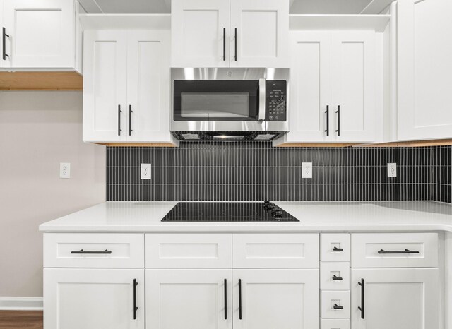 2539 Rafiki Dr, Clarksville, TN 37042 - kitchen with stainless steel microwave, black electric cooktop, white cabinetry, light countertops, and decorative backsplash
