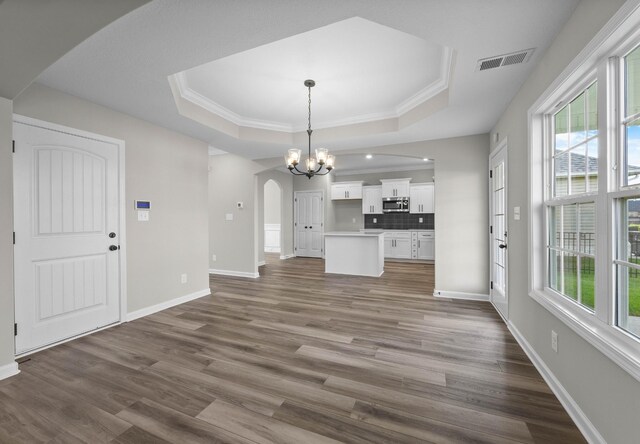 2539 Rafiki Dr, Clarksville, TN 37042 - unfurnished living room with arched walkways, a raised ceiling, a chandelier, dark wood-type flooring, and crown molding