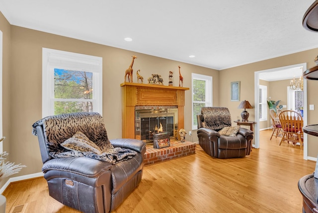 living area featuring visible vents, an inviting chandelier, light wood-style flooring, a brick fireplace, and baseboards