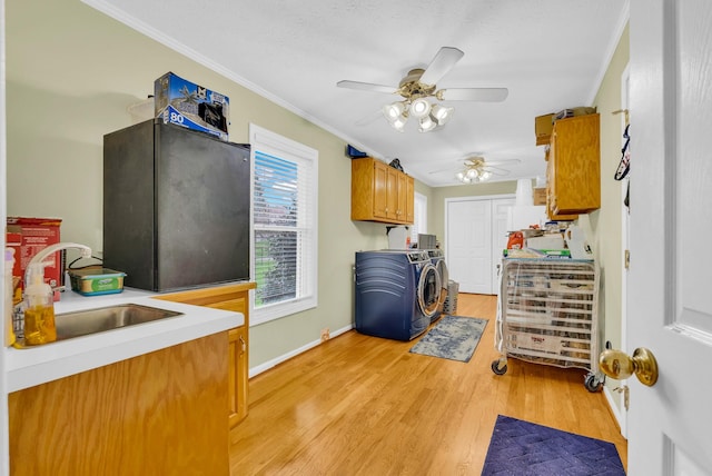 clothes washing area featuring light wood-style flooring, a sink, separate washer and dryer, crown molding, and ceiling fan