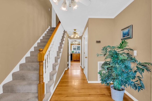 hall with baseboards, stairs, ornamental molding, and light wood-type flooring