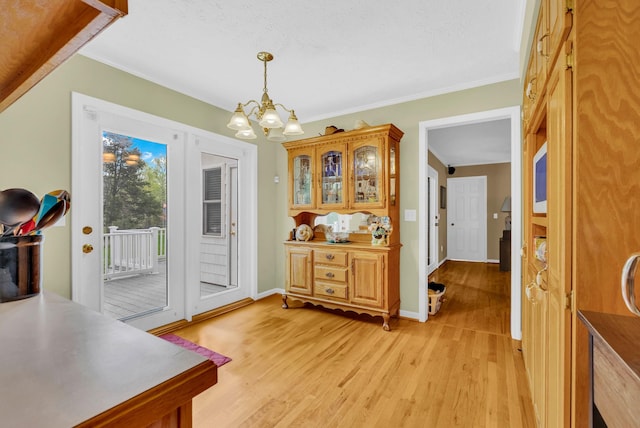interior space with a chandelier, light wood-style flooring, crown molding, and baseboards