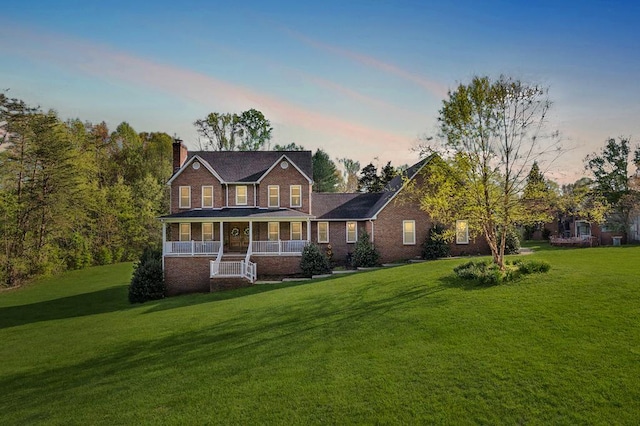 view of front of home with covered porch, a yard, a chimney, and brick siding