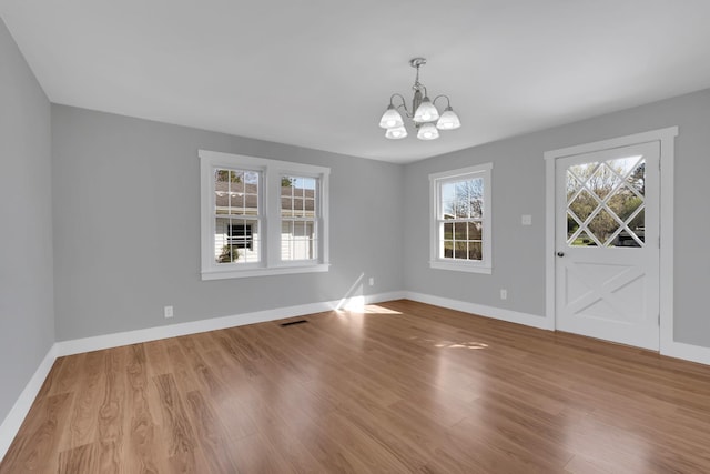 unfurnished dining area with baseboards, a notable chandelier, visible vents, and wood finished floors