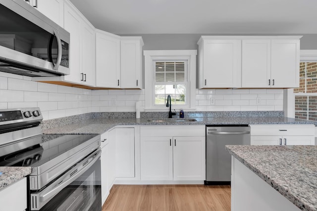 kitchen with a sink, white cabinets, light wood-style floors, and appliances with stainless steel finishes