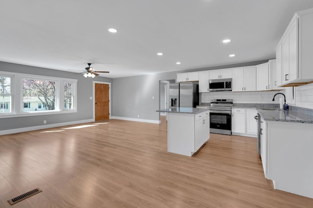 kitchen featuring decorative backsplash, visible vents, stainless steel appliances, a sink, and a center island