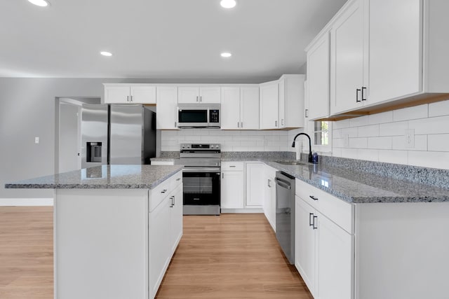 kitchen with stainless steel appliances, a center island, decorative backsplash, a sink, and light wood finished floors