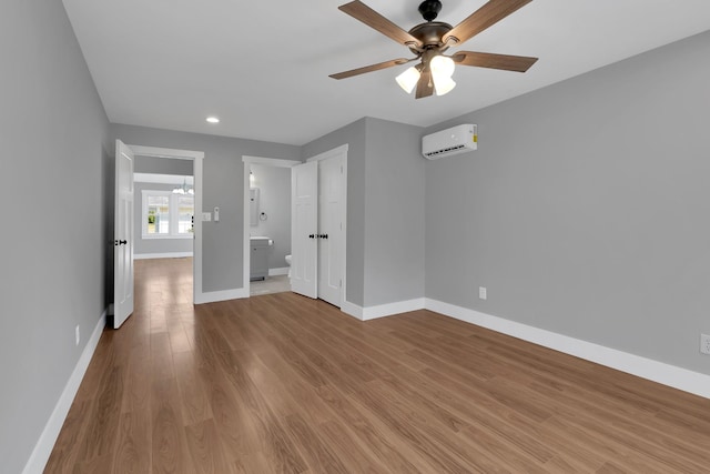 interior space featuring a wall mounted air conditioner, baseboards, ensuite bathroom, and wood finished floors