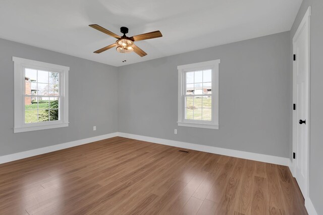 empty room featuring a ceiling fan, visible vents, baseboards, and wood finished floors