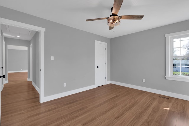 spare room featuring a ceiling fan, baseboards, attic access, and wood finished floors