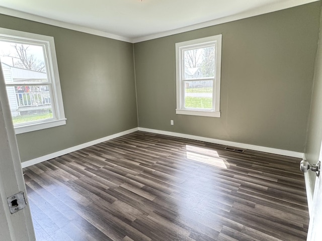 empty room featuring ornamental molding, dark wood-type flooring, baseboards, and visible vents