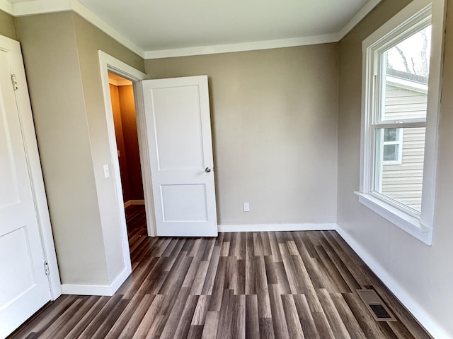 empty room featuring dark wood-style flooring, baseboards, and visible vents