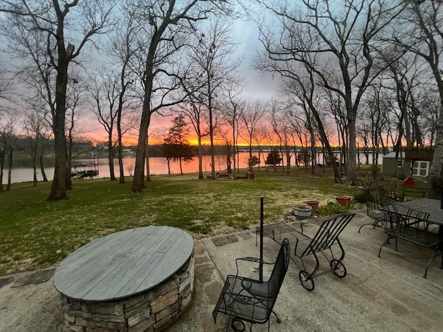 patio terrace at dusk featuring an outdoor fire pit, a yard, and a water view