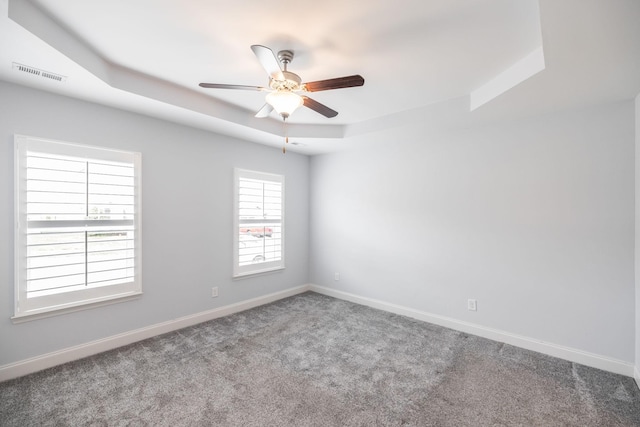 unfurnished room featuring a tray ceiling, carpet floors, baseboards, visible vents, and ceiling fan