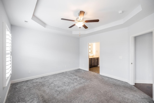 unfurnished bedroom with ensuite bathroom, carpet, baseboards, a ceiling fan, and a raised ceiling