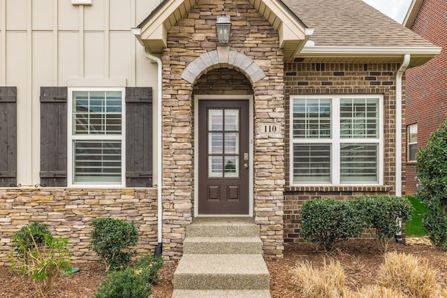 property entrance with a shingled roof, stone siding, and board and batten siding