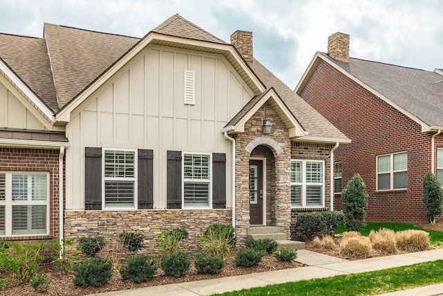 view of front of home featuring stone siding, a chimney, board and batten siding, and roof with shingles
