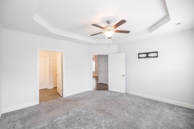 unfurnished bedroom featuring a tray ceiling, baseboards, visible vents, and carpet