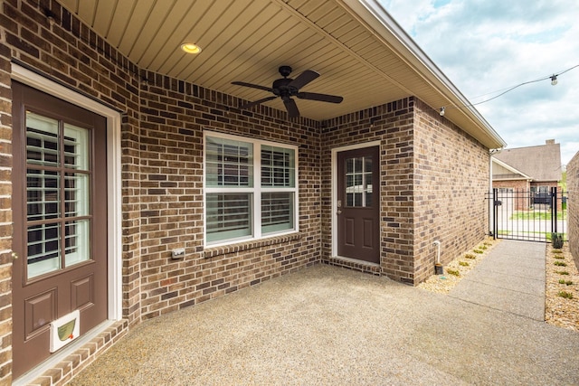 entrance to property with fence, a gate, ceiling fan, brick siding, and a patio area