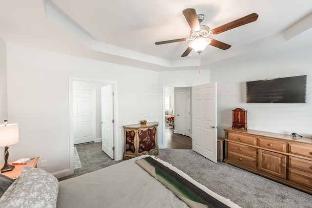 carpeted bedroom with a tray ceiling, baseboards, and a ceiling fan