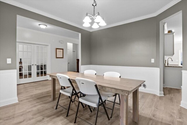 dining area featuring french doors, ornamental molding, an inviting chandelier, and light wood-type flooring