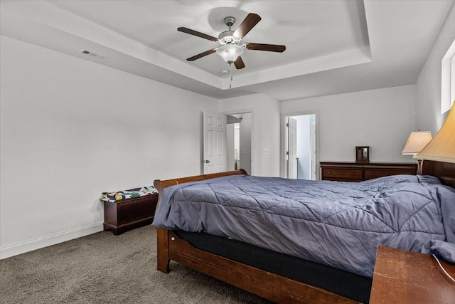 carpeted bedroom with a ceiling fan, a tray ceiling, baseboards, and visible vents