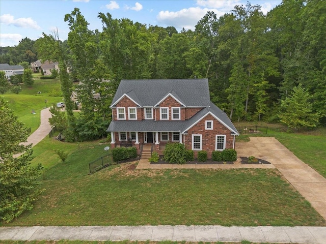 view of front of property with fence, brick siding, a front lawn, driveway, and covered porch