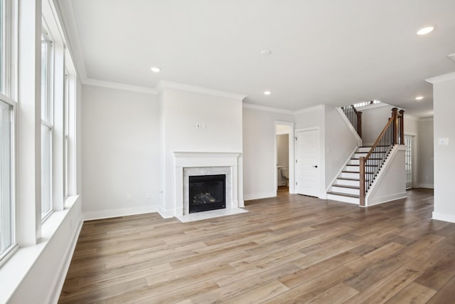 unfurnished living room with a premium fireplace, crown molding, stairs, and wood finished floors