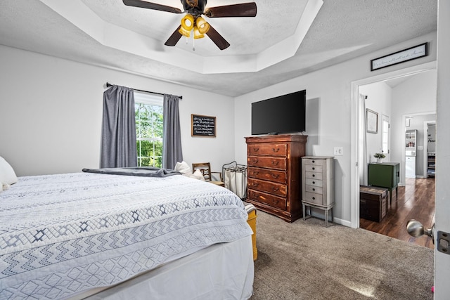carpeted bedroom featuring a raised ceiling, baseboards, ceiling fan, and a textured ceiling