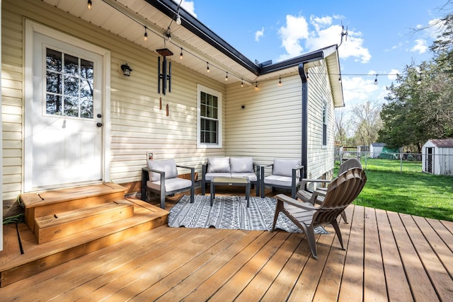 wooden terrace with outdoor lounge area, an outbuilding, fence, and a lawn
