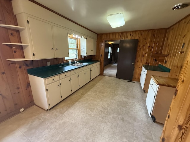 kitchen with a sink, white cabinetry, wooden walls, visible vents, and dark countertops