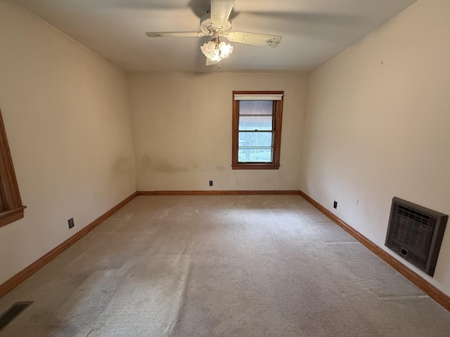spare room featuring light colored carpet, baseboards, visible vents, heating unit, and a ceiling fan