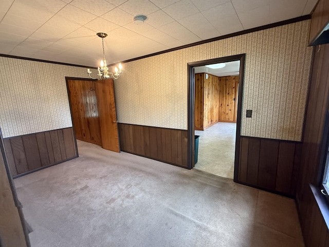 carpeted empty room featuring crown molding, wallpapered walls, and wainscoting