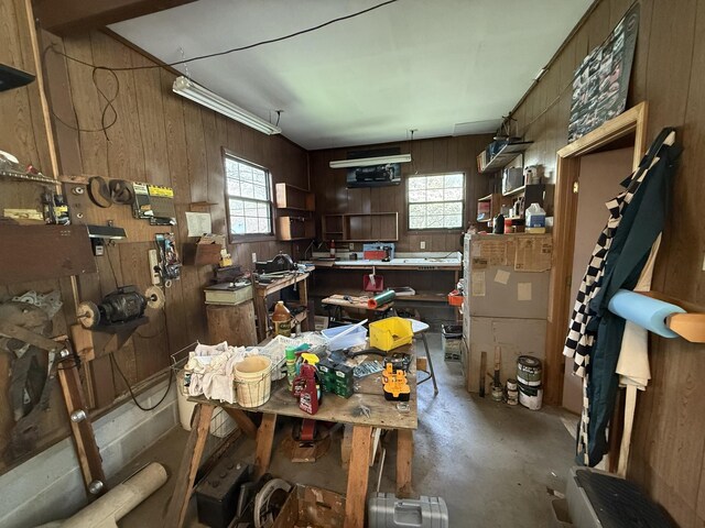 miscellaneous room with concrete flooring, wooden walls, a healthy amount of sunlight, and a workshop area