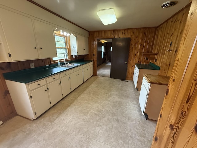 kitchen featuring white cabinetry, crown molding, wood walls, a sink, and dark countertops