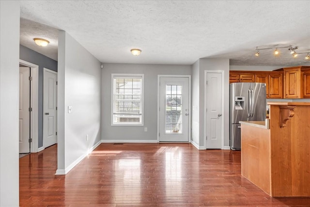 interior space featuring stainless steel refrigerator with ice dispenser, baseboards, a textured ceiling, brown cabinetry, and wood finished floors