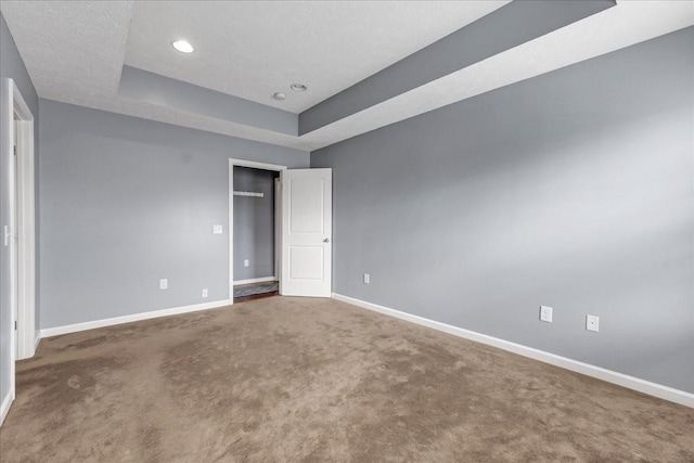 spare room with a raised ceiling, carpet, baseboards, and recessed lighting