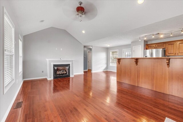 unfurnished living room with vaulted ceiling, wood-type flooring, ceiling fan, visible vents, and a fireplace