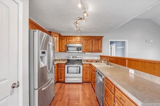 kitchen featuring a textured ceiling, appliances with stainless steel finishes, a sink, light wood-type flooring, and brown cabinetry